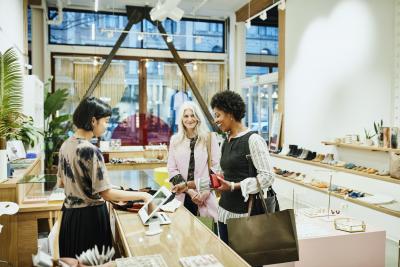 Laughing woman looking at shirt while checking out after shopping in boutique with friend