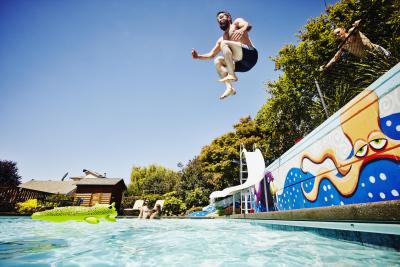 Man jumping from wall into outdoor pool with friends watching in background
