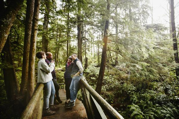 Woman taking digital photo with smartphone of couple while hiking on bridge in rainforest