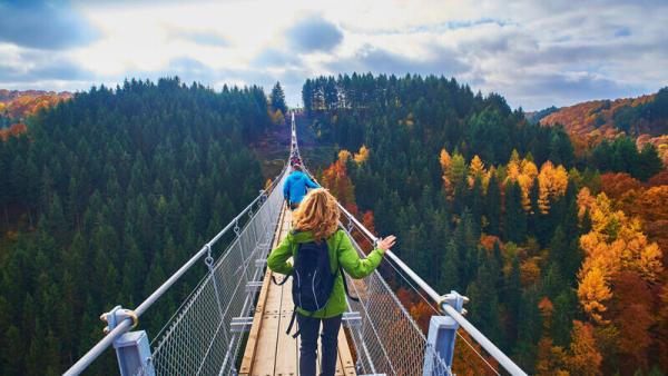 Image showing people walking across a narrow bridge towards a forested hilltop