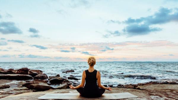 Image of a person sat in a yoga pose by the sea