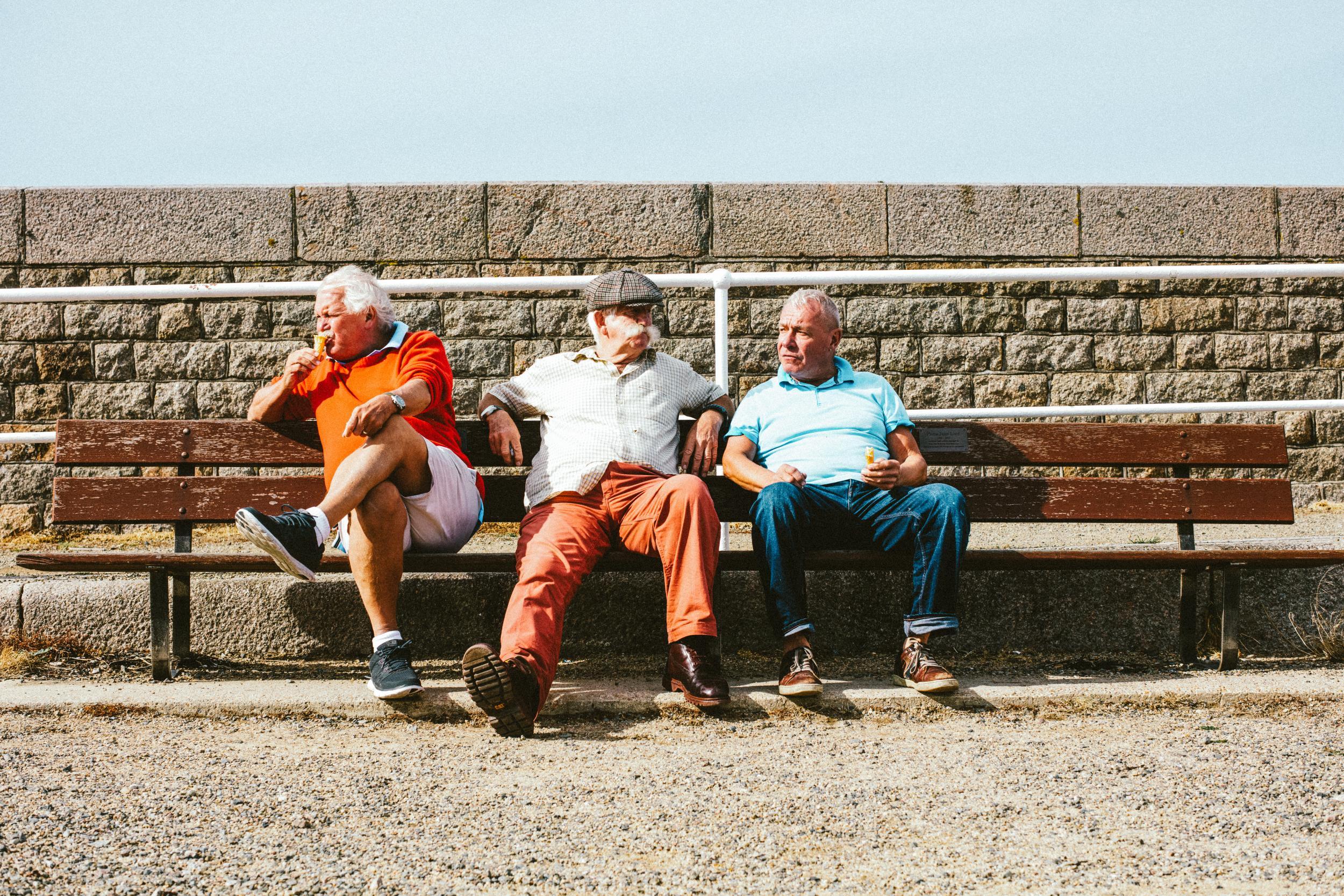 three old men sit on bench talking to each-other