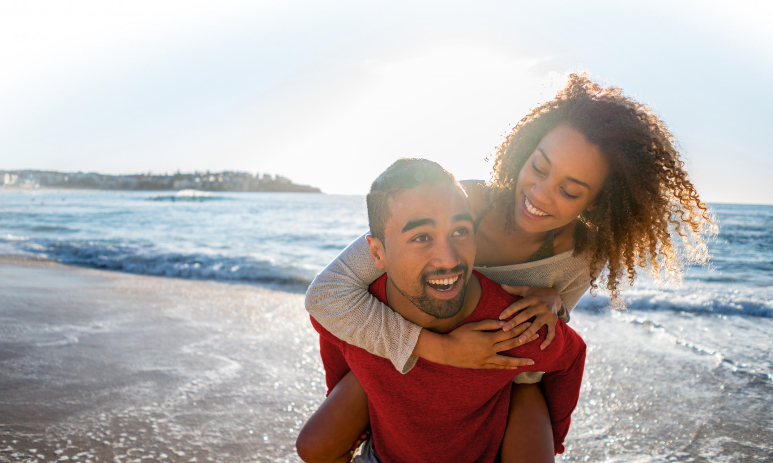 Happy loving couple walking at the beach and man carrying his girlfriend on a piggyback ride