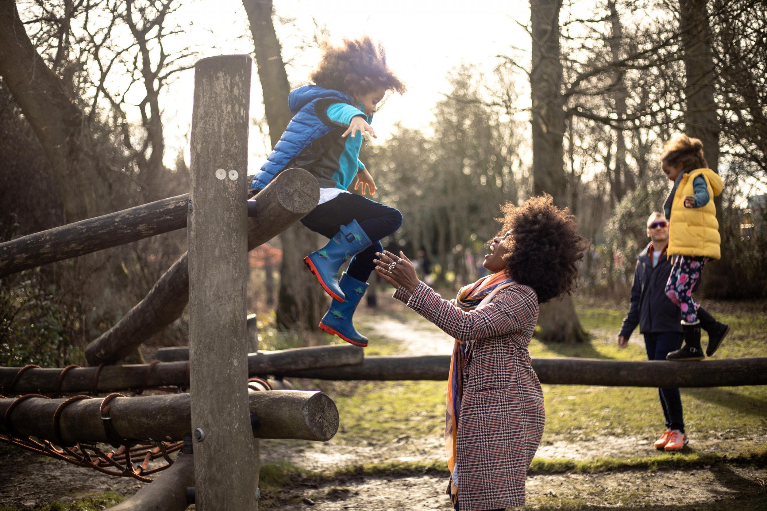 A young boy jumping into his mother's arms off a wooden play area.