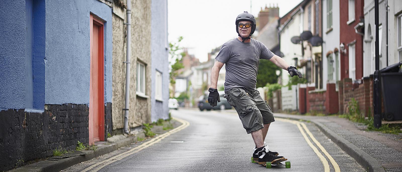 644646899 A 50 year old long boarder riding his long board along a quiet urban street.